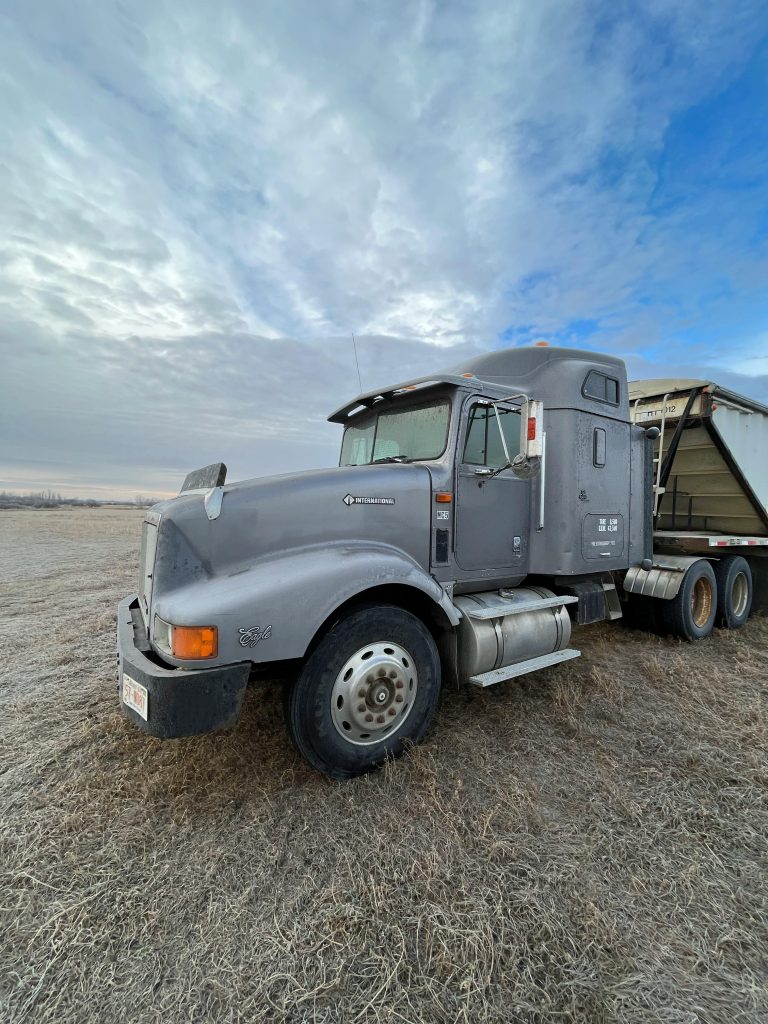 A robust semi-truck parked on a dry grass field beneath a vast blue sky, showcasing industrial strength and rural simplicity.